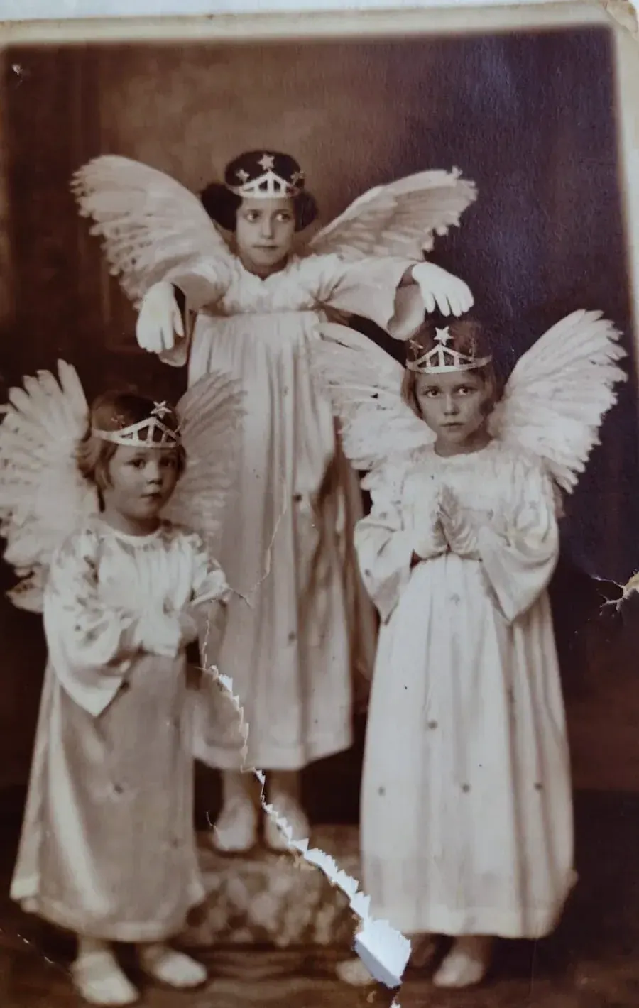Fotografia antiga em sépia de três crianças vestidas de anjo, com asas e coroas de estrelas