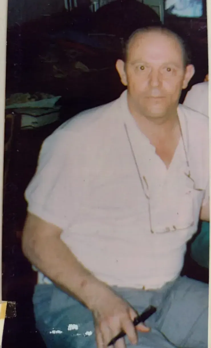 Pedro de camisa polo branca com óculos pendurados no colarinho, sentado, segurando uma caneta